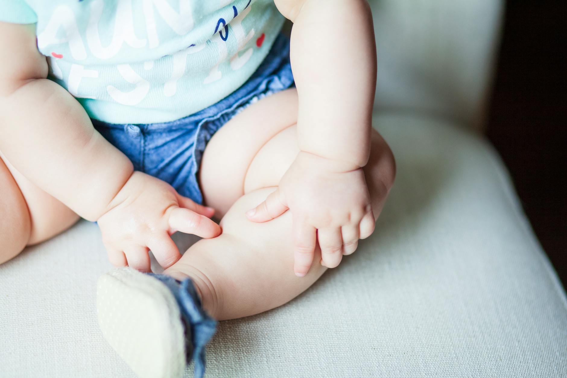 baby wearing green shirt and blue shorts sitting on gray chair